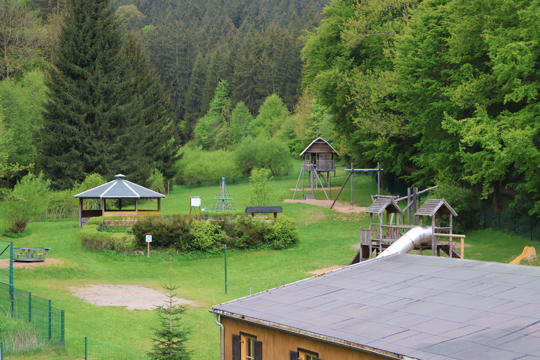 Blick auf den Spielplatz mit Grillhütte, Seilbahn, Karussell und Spielhütte.
