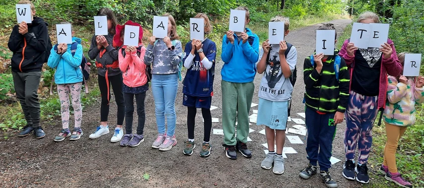 Gruppe von Kindern, die Buchstabenschilder halten und das Wort Waldarbeiter darstellen